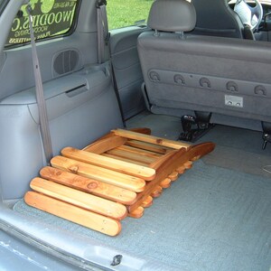 May include: A wooden folding chair is in the back of a gray minivan. The chair is folded and stacked in the cargo area. The chair is made of natural wood and has a light brown color.
