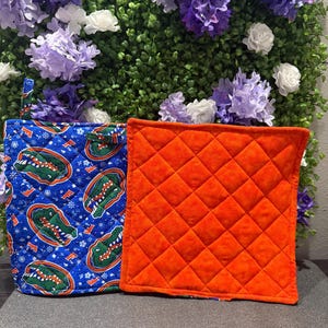 May include: Two quilted pot holders. One is blue with a white snowflake pattern and an alligator logo. The other is solid orange.