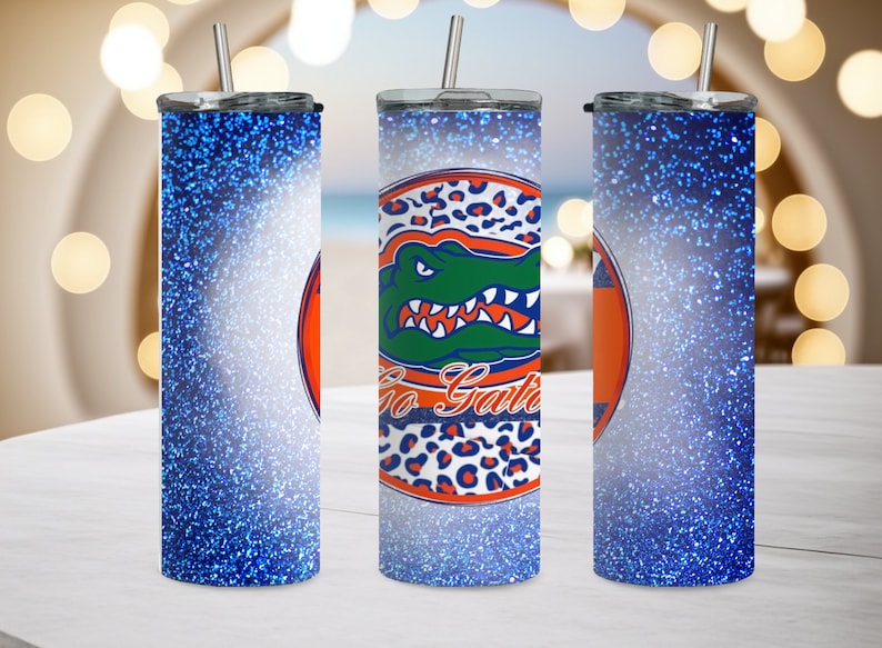 May include: Three stainless steel tumblers with blue glitter designs. The center tumbler features a green alligator with the words "Go Gators" in a white circle with orange and black leopard print accents.