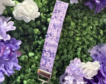 May include: A purple and white floral patterned key chain with a silver key ring.
