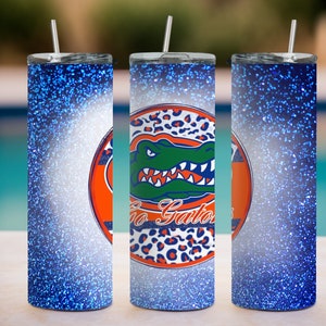 May include: Three stainless steel tumblers with blue glitter finish. The center tumbler features a white and orange circle with a green alligator and the text "Go Gators".