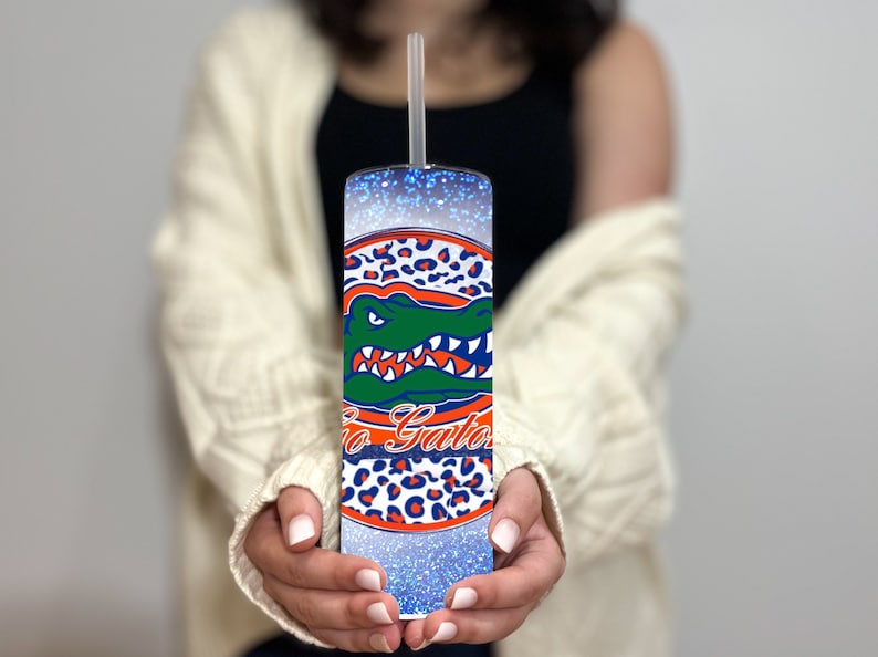 May include: A blue and white tumbler with a glitter finish and a University of Florida Gators logo. The logo features an alligator with the words "Go Gators" in orange and blue.