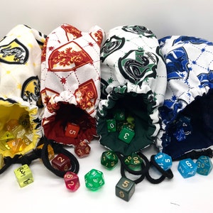 May include: Four drawstring dice bags with different house crest patterns. The bags are white with repeating patterns of yellow, red, green, and blue crests. Each bag is open, revealing dice in various colors.