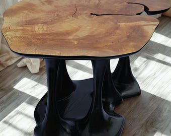 May include: A distinctive coffee table featuring a natural wood grain top and a black, sculptural base. The table's top is approximately 122 cm long and 91 cm wide, with a live edge design. The base has an organic, flowing shape.