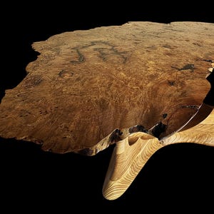 Könnte beinhalten: Ein Holztisch mit lebendiger Kante und natürlicher, unregelmäßiger Form. Die Tischplatte hat eine warme braune Farbe mit komplizierten Maserungsmustern. Der Tisch wird von einem hellen, geformten Holzfuß getragen.