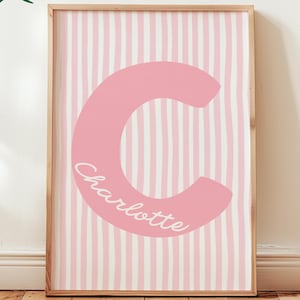May include: A framed pink and white striped print featuring a large pink letter "C" with the name "Charlotte" in cursive. The print is displayed on a wooden floor. The words "Custom Digital Download" and "Cherry Blossom" are also visible.