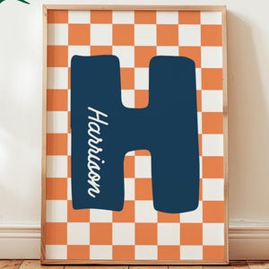 Pode incluir: Impressão emoldurada com uma grande letra "H" azul marinho e o nome "Harrison" em itálico. O fundo tem um padrão xadrez laranja e branco. As palavras "Custom Digital Download" estão em uma bolha verde.