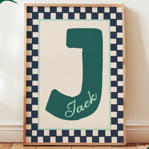 Puede incluir: Una impresión artística enmarcada con una gran letra "J" de color verde azulado con el nombre "Jack" en cursiva. La obra de arte tiene un fondo crema con un borde verde azulado y un marco a cuadros azul marino y blanco. El texto inferior dice "Ocean, Misty Jade & Twilight."