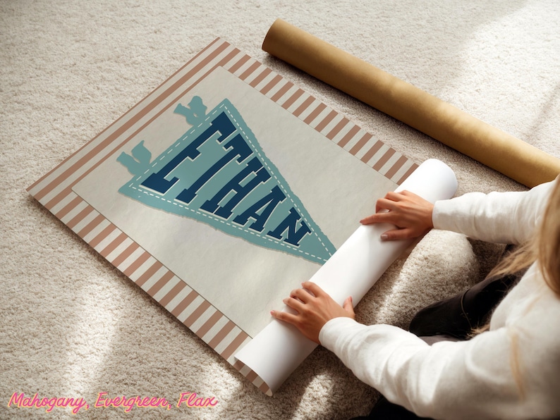 May include: A personalised pennant-style print with the name "ETHAN" in blue lettering. The print has a light blue pennant shape with a white border and is set against a cream background with a striped border. A rolled-up poster is next to the print.
