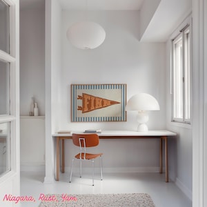 May include: A minimalist home office with white walls and flooring. It features a wooden desk, an orange chair, and a framed pennant reading "FINN". A white lamp and a pendant light provide illumination. The room has a modern aesthetic.