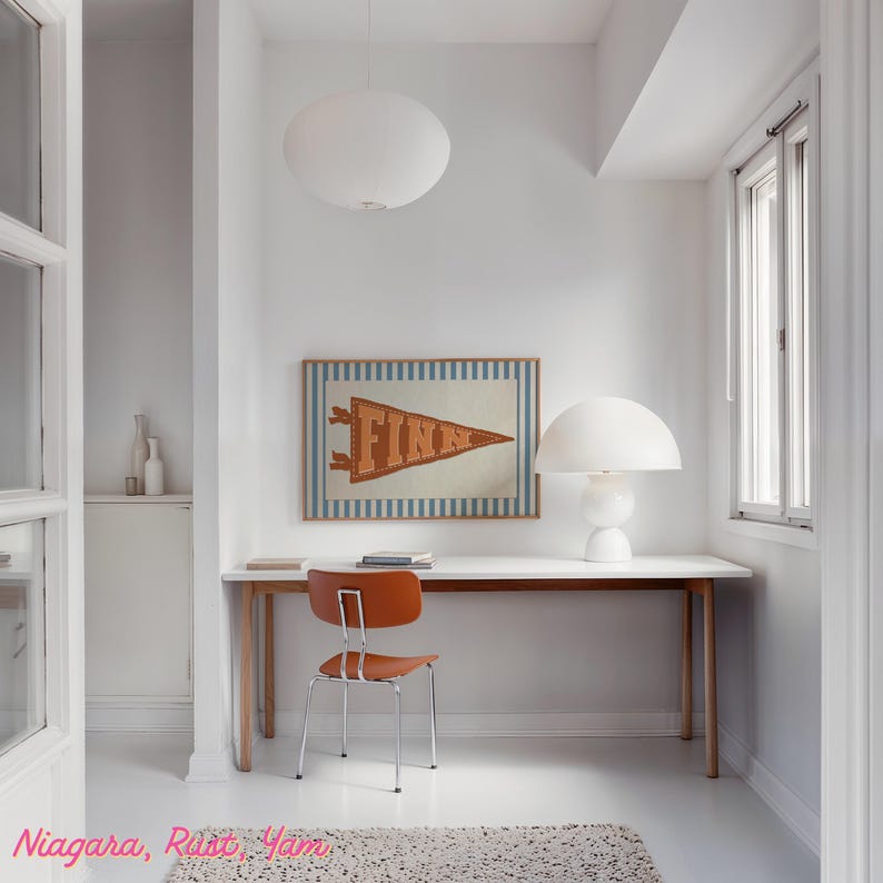 May include: A minimalist home office with white walls and flooring. It features a wooden desk, an orange chair, and a framed pennant reading "FINN". A white lamp and a pendant light provide illumination. The room has a modern aesthetic.