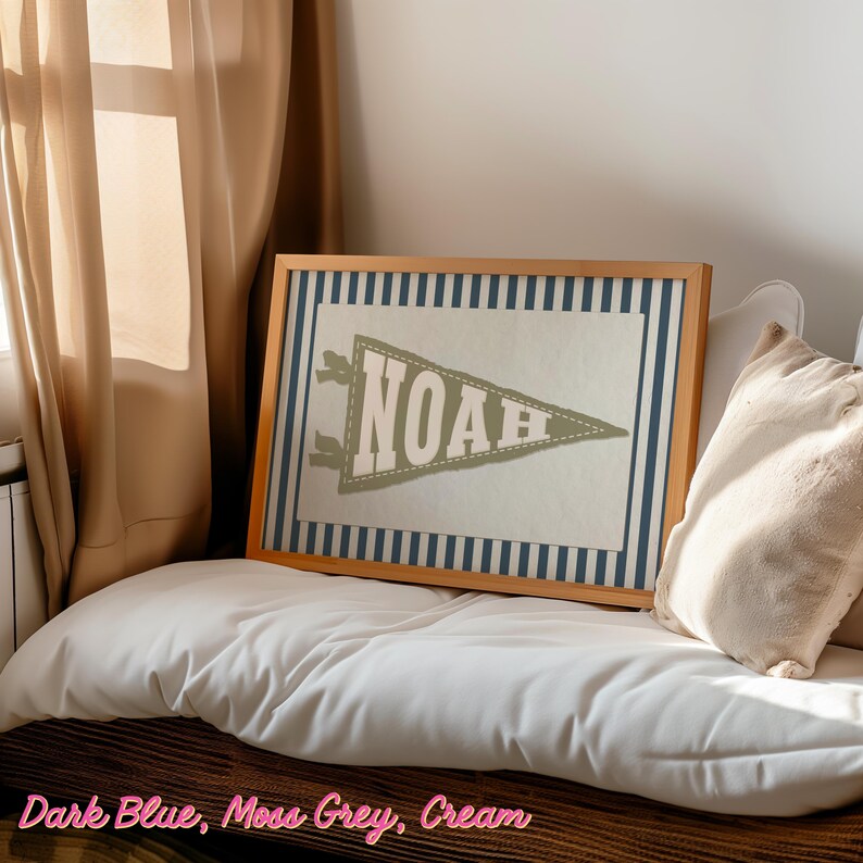 May include: A framed print with a pennant design displaying the name "NOAH" in moss grey. The pennant is set against a cream background with a dark blue striped border, within a wooden frame. The text "Dark Blue, Moss Grey, Cream" is at the bottom.