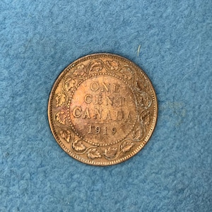 Może przedstawiać: Kanadyjska moneta jednocentowa z 1919 roku wykonana z miedzi. Na monecie widnieje napis "ONE CENT CANADA 1919" otoczony ozdobnym brzegiem.