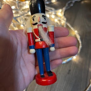 May include: A wooden nutcracker figurine with a black hat, white beard, red and blue uniform, and a red base.