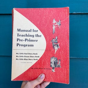 May include: A vintage book titled "Manual for Teaching the Pre-Primer Program" with a red cover and white text. The book includes the titles "My Little Red Story Book", "My Little Green Story Book", and "My Little Blue Story Book".