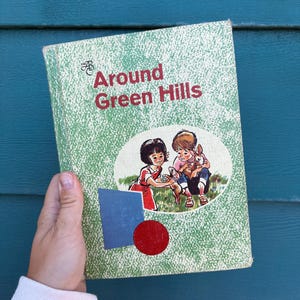May include: A vintage children's book titled "Around Green Hills" with a green speckled cover. The cover features illustrations of two children and a rabbit. The title is in red, and there is a blue square and red circle on the cover.