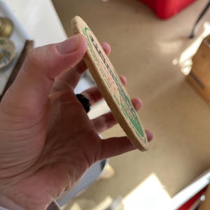 May include: A round, brown cardboard coaster with a green border and white text. The text reads "Budweiser" and "King of Beers".