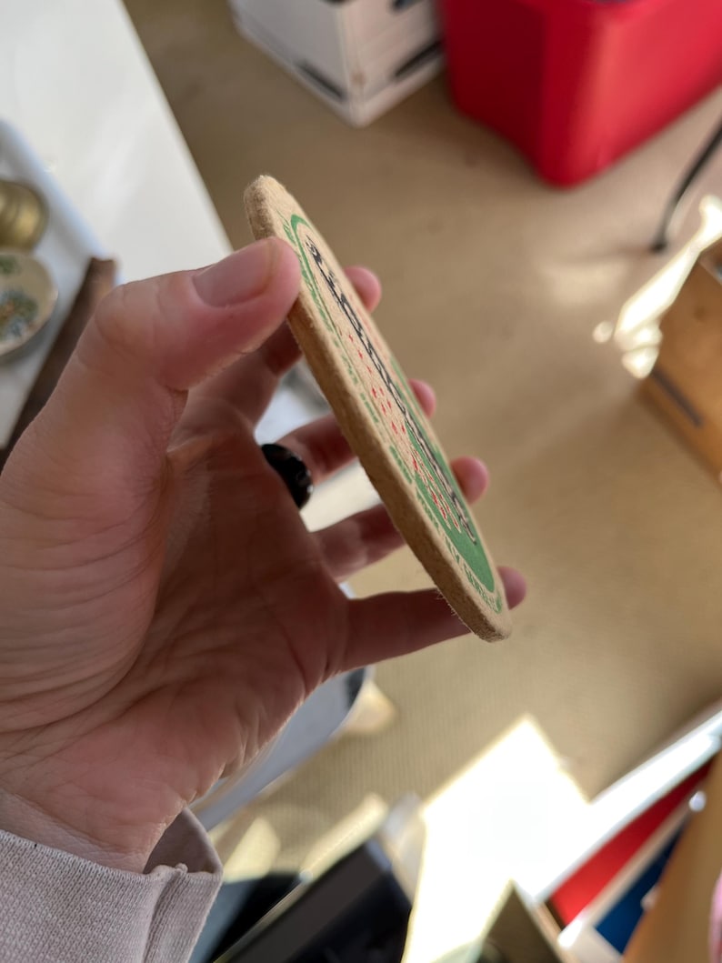 May include: A round, brown cardboard coaster with a green border and white text. The text reads "Budweiser" and "King of Beers".