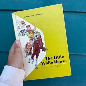 May include: Vintage children's book titled "The Little White House" with a yellow cover. The cover illustration depicts a boy on a brown horse, with a white house in the background. The book is part of "The Ginn Basic Readers" series.