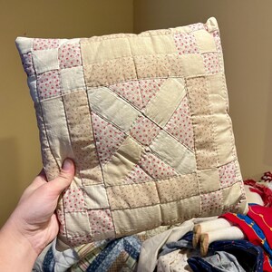 May include: A handmade patchwork pillow with a cream and pink floral pattern. The pillow is made of squares of fabric sewn together to create a geometric design.
