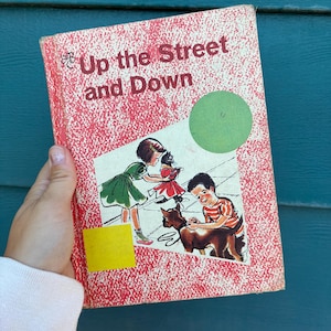 May include: Vintage children's book titled "Up the Street and Down" with a red cover and illustrations of children and a dog. The cover has a white rectangle with a green circle and yellow square.