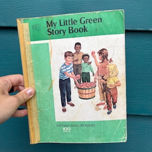 May include: Vintage children's book titled "My Little Green Story Book" with a green cover. The cover illustration depicts children around a basket of apples. The book is from "The Ginn Basic Readers" series, 100th edition.