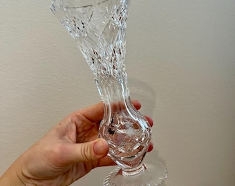 May include: A clear glass vase with a cut crystal design. The vase has a round base and a tall, slender neck.