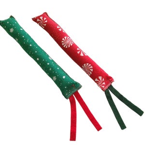 May include: Two long, cylindrical cat toys. One is green with white snowflakes, the other is red with white peppermint candies. Both have matching ribbon tassels at the ends. These toys are designed for feline play.