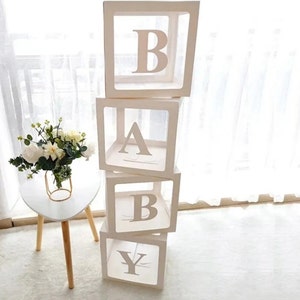 May include: Four white boxes stacked on top of each other, each with a clear front and a letter of the word "BABY" printed on the front. The boxes are made of cardboard and are decorated with a white ribbon.