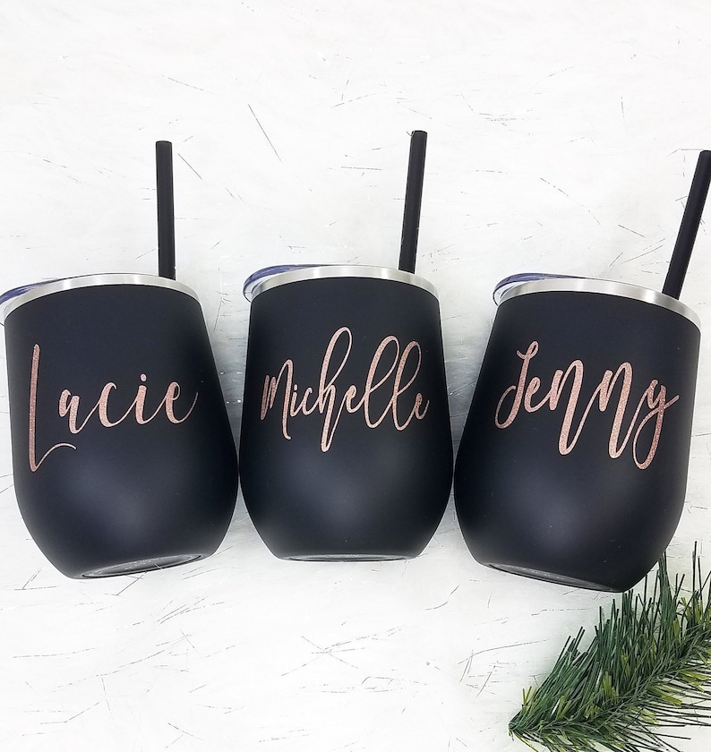 Puede incluir: Tres vasos de acero inoxidable negro con letras doradas. Los vasos est&aacute;n personalizados con los nombres "Lacie", "Michelle" y "Jenny".