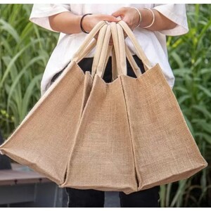 May include: Three brown burlap tote bags with thick rope handles. The bags are made of natural jute fabric and are perfect for carrying groceries or other items.