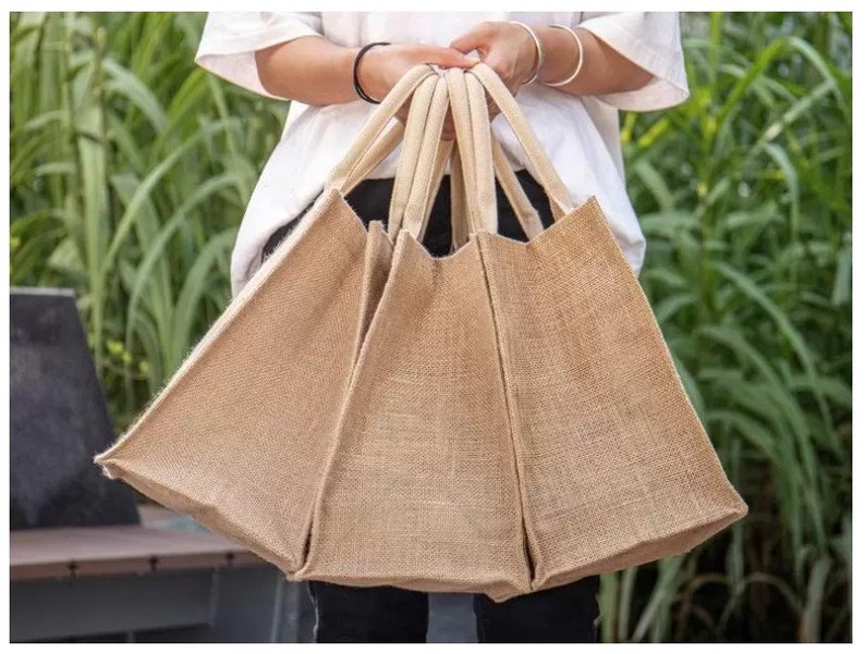 May include: Three brown burlap tote bags with thick rope handles. The bags are made of natural jute fabric and are perfect for carrying groceries or other items.