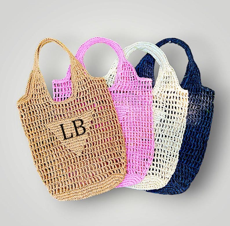 May include: Four crocheted tote bags in different colors: beige, pink, white, and navy blue. The beige bag has the initials "LB" embroidered on it.