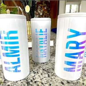 K&ouml;nnte beinhalten: Drei wei&szlig;e isolierte Becher mit schimmerndem blauen Schriftzug. Die Becher sind mit "ALMIR", "NATALIE" und "MARY" beschriftet.