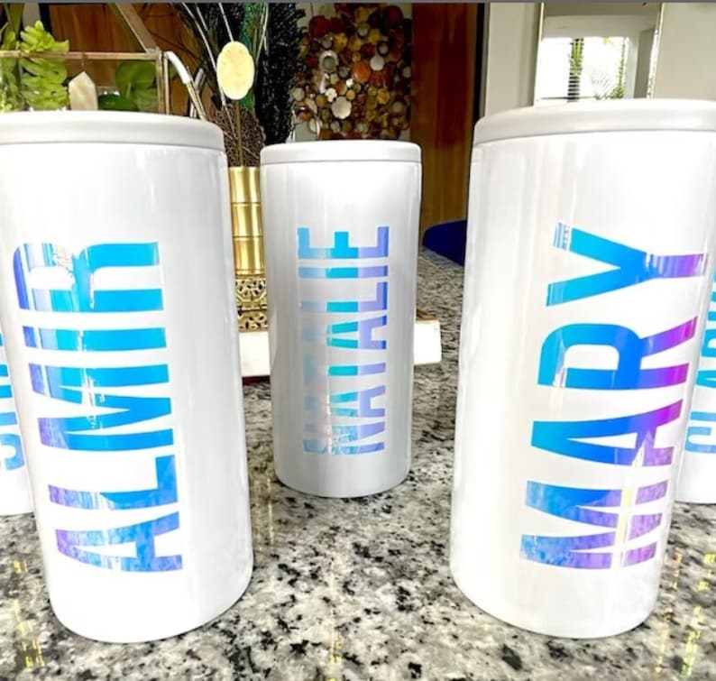 K&ouml;nnte beinhalten: Drei wei&szlig;e isolierte Becher mit schimmerndem blauen Schriftzug. Die Becher sind mit "ALMIR", "NATALIE" und "MARY" beschriftet.