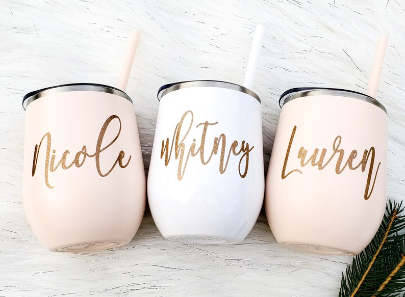 Puede incluir: Tres vasos de vino de acero inoxidable personalizados con letras doradas. Los vasos son rosa, blanco y rosa. Los nombres en los vasos son Nicole, Whitney y Lauren.