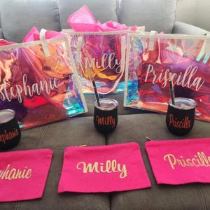 May include: A collection of personalized gifts, including iridescent tote bags, black tumblers with straws, and pink cosmetic bags. Each item is inscribed with a name in a cursive font, creating a cohesive set.