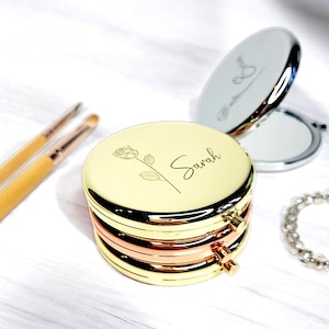 May include: A gold compact mirror with a rose design and the name "Sarah" engraved on the lid. The mirror is open and shows a reflection.