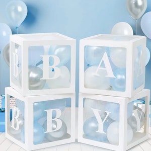 May include: Four white boxes with clear sides, each containing blue and white balloons. The boxes are stacked in a pyramid shape, with the top box spelling the letter "A" and the bottom boxes spelling "BABY".
