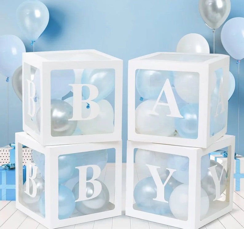 May include: Four white boxes with clear sides, each containing blue and white balloons. The boxes are stacked in a pyramid shape, with the top box spelling the letter "A" and the bottom boxes spelling "BABY".