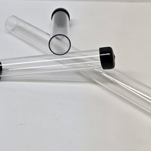 Puede incluir: Tres tubos de plástico transparente con tapas negras. Los tubos están sobre una superficie blanca.