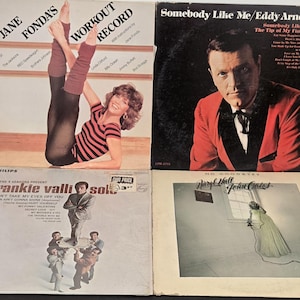 May include: Three vinyl record albums. The first album is a workout record featuring Jane Fonda. The second album is a Frankie Valli record. The third album is a Daryl Hall and John Oates record.