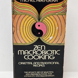 Pode incluir: Um livro de bolso intitulado Zen Macrobiotic Cooking de Michel Abehsera. A capa apresenta um símbolo yin-yang em preto e branco rodeado por linhas circulares concêntricas laranja, amarelas e verdes. O texto inclui o nome do autor.