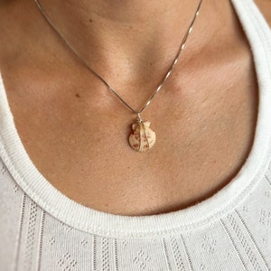 May include: A silver chain necklace with a seashell pendant. The seashell is a light brown color with red markings.