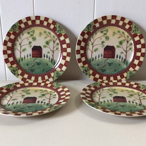 May include: Set of four decorative plates with a country landscape design. Each plate features a red house on a green hill, surrounded by trees, with a red and cream checkered border.