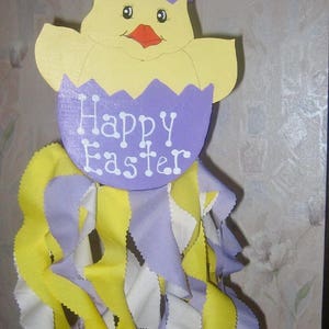 May include: A purple and yellow wooden chick with the text "Happy Easter" hanging from a purple, yellow, and white fabric streamer.