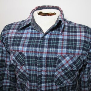 May include: A blue, green, and red plaid flannel shirt with two chest pockets and button fastenings. The shirt has a quilted collar and is displayed on a mannequin.