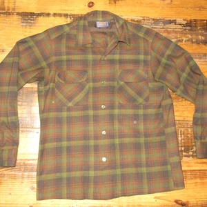 May include: A long-sleeved plaid shirt in shades of green, brown, and gray. The shirt has two chest pockets, a button-down front, and buttoned cuffs. The collar is a classic spread style.