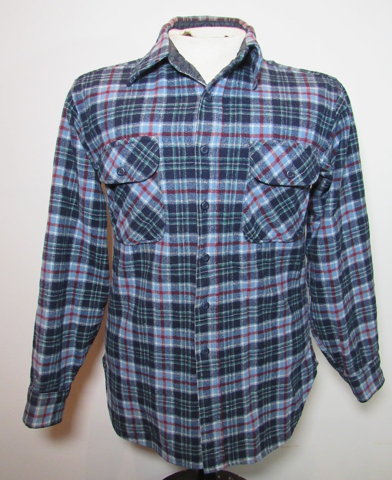 May include: A blue, red, and green checked flannel shirt with two chest pockets and button fastenings. The long-sleeved shirt is displayed on a mannequin, showcasing the classic pattern and design.