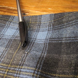 K&ouml;nnte beinhalten: Nahaufnahme eines blau-schwarz karierten Stoffes mit gelben Linien. Ein schwarzer Stift mit silberner Spitze liegt auf dem Stoff. Der Stoff hat eine gewebte Textur und ein klassisches Muster.